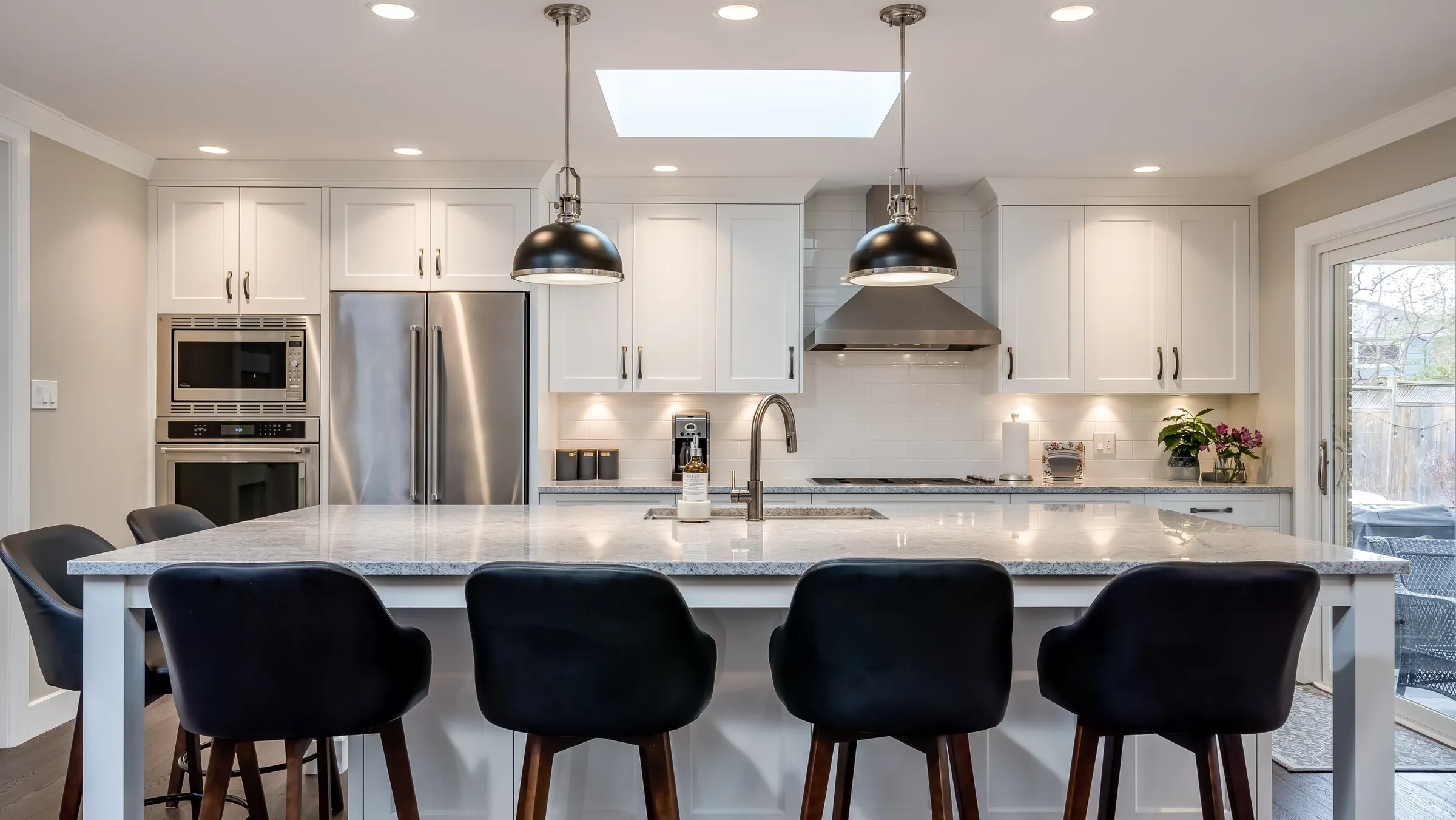 Bright white kitchen with a long island and black bar stools